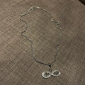 Silver infinity necklace on a brown textured fabric background